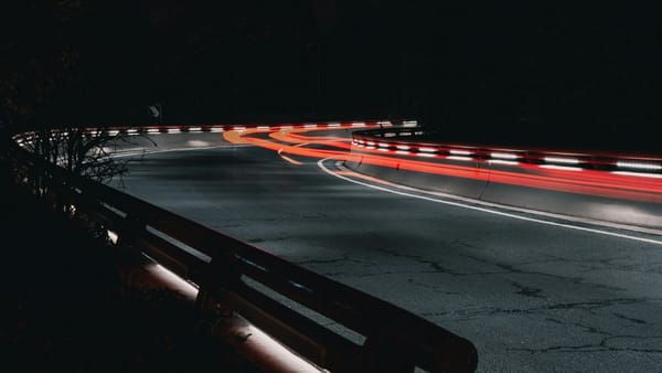 Fast-moving lights on a dark road curve—showing policy moving too fast for ethics to keep up.