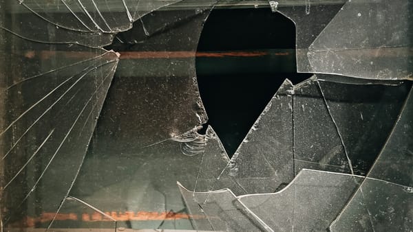 A pane of glass fractured with sharp cracks and a hollow center, symbolising fragile systems that appear solid until they break.
