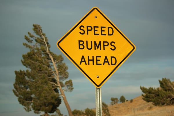 Yellow road sign reading “Speed Bumps Ahead,” symbolising intentional friction as a safeguard in system design.